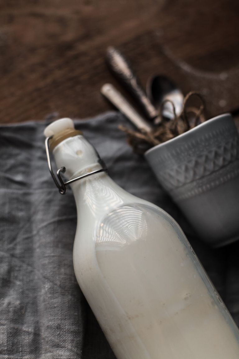 Close-up of a milk bottle beside a ceramic cup and cutlery on a wooden table.